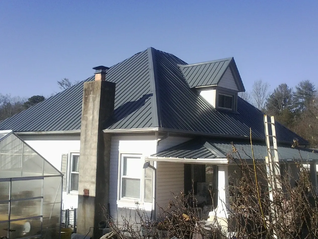 Dark blue standing seam metal roof on a white farmhouse with dormer — Slate & Tile Roof Repair by Roofing Brothers in Owens Cross Roads