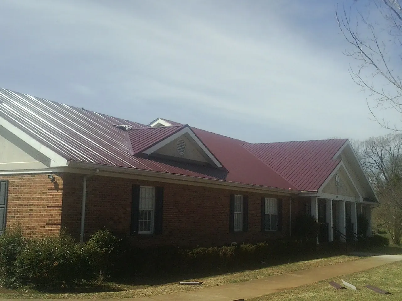 Red metal roof with gabled entries on a long brick building, from a Hail Damage Roof Repair job in Owens Cross Roads
