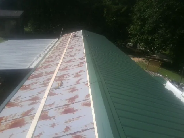 Old rusted panels beside newly installed green metal roofing — Wind Damage Roof Repair by Roofing Brothers in Owens Cross Roads