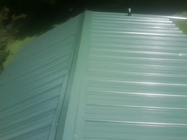 New green metal panels meeting at the ridge of a roof — Flat Roof Repair work by our crew in Owens Cross Roads