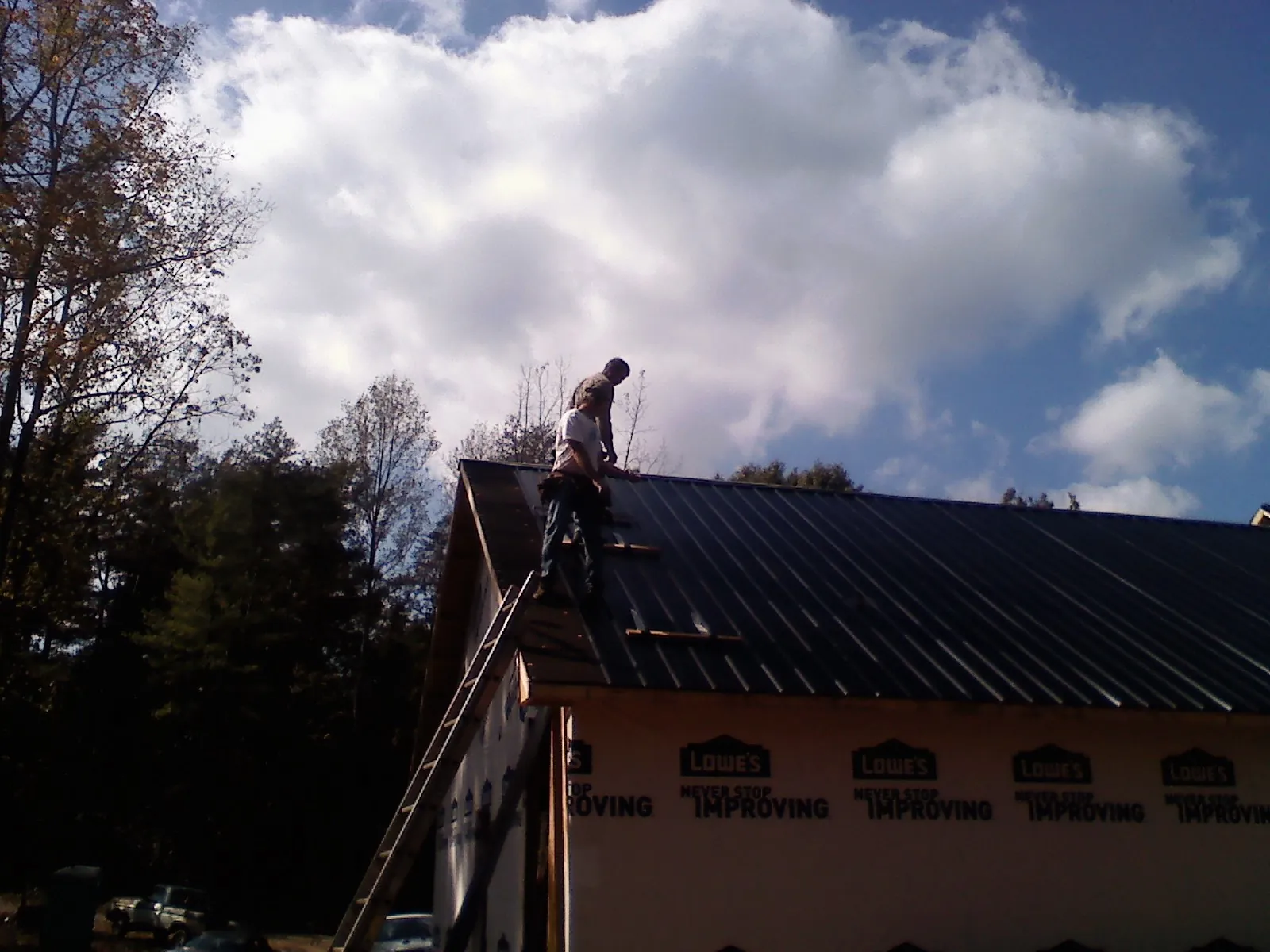 Roofer fastening dark metal panels high against a cloudy sky, from a Roof Inspection job in Owens Cross Roads