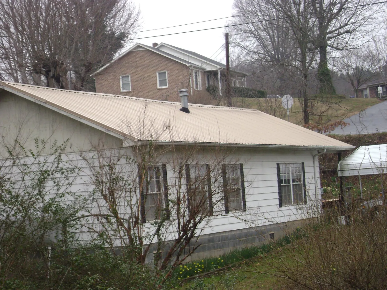 Tan metal roof on a white sided house set into a hillside — Commercial Roofing by Roofing Brothers in Owens Cross Roads