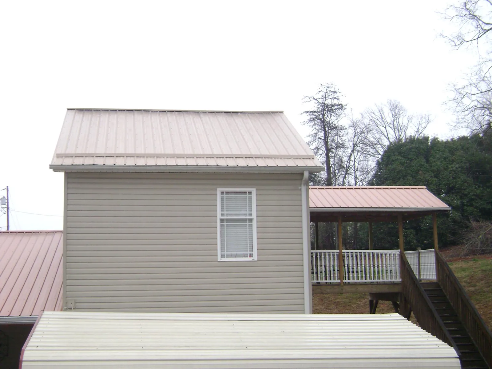 Tan metal roofs on a two story addition and attached porch, from a Roof Replacement job in Owens Cross Roads
