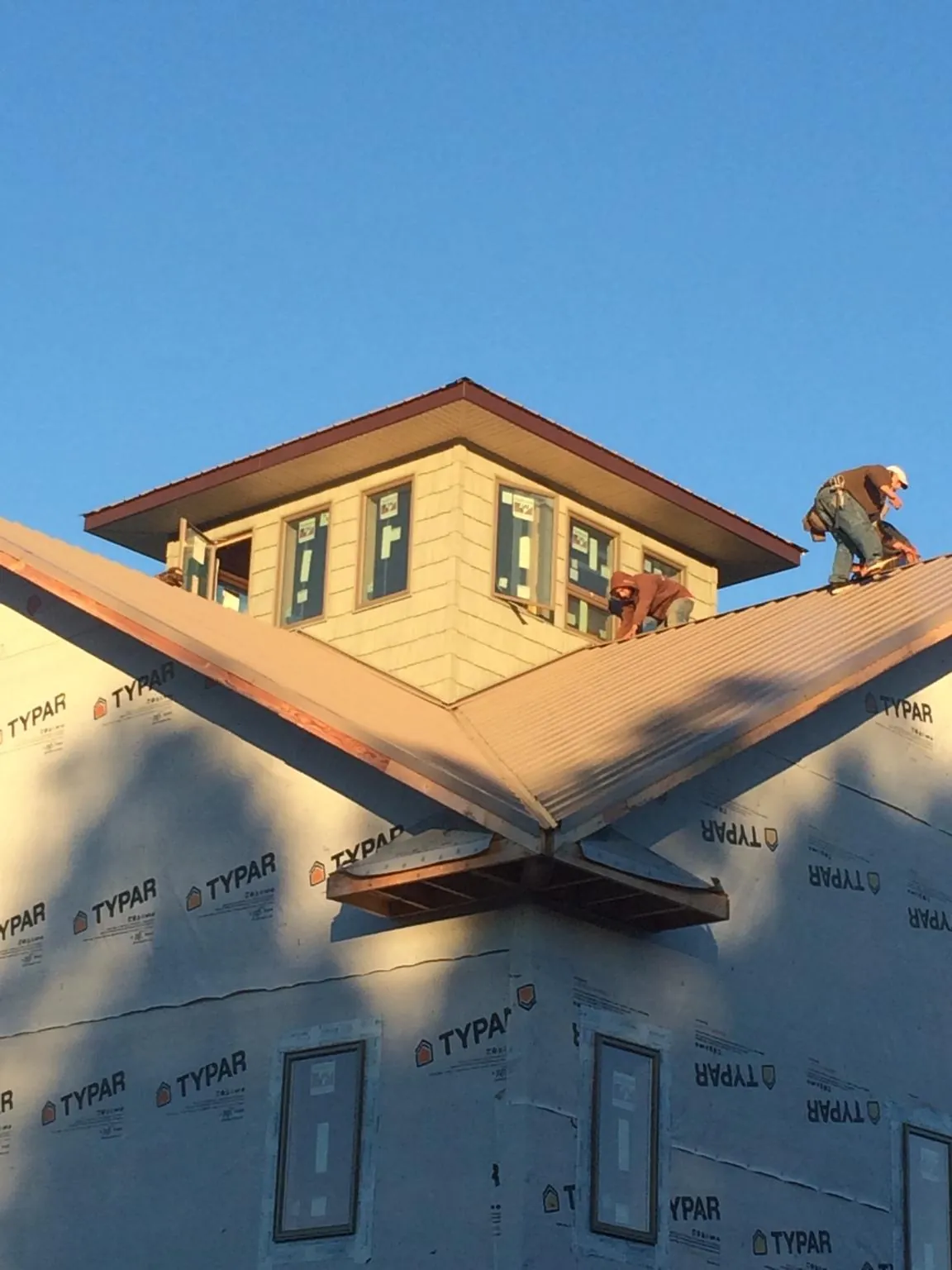 Roofers working around a rooftop cupola on a new metal roof at sunset — Roof Waterproofing in Owens Cross Roads by Roofing Brothers